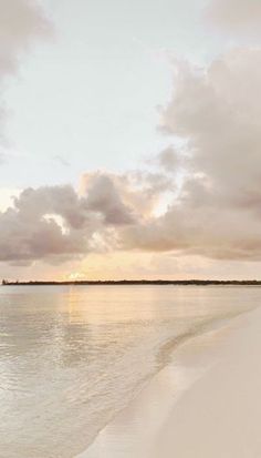 the sun is setting on an empty beach with water and land in the background,