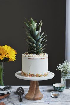 a white cake with sprinkles and a pineapple sitting on top of it