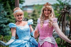 two women dressed as princesses standing next to each other in front of a fence