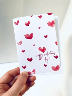 someone holding up a valentine's day card with red hearts on white paper that says happy valentine's day