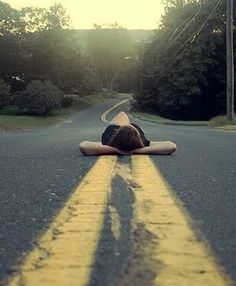 a person laying on their back in the middle of an empty road with trees and bushes behind them