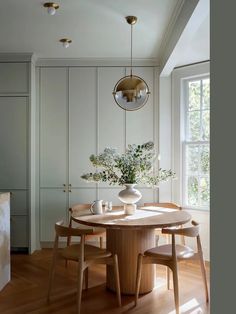 a dining room table with four chairs and a vase on the table in front of it