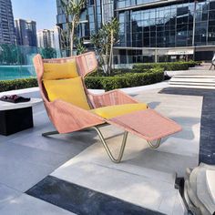 a lounge chair sitting on top of a cement floor next to a swimming pool in front of tall buildings