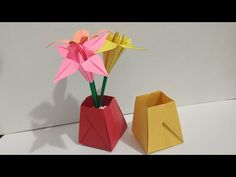 two origami flowers in a red vase next to an open yellow paper bag