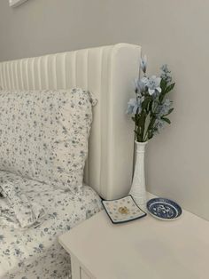 a white bed with blue flowers in a vase on the end table next to it