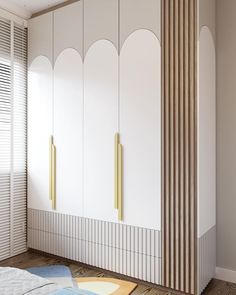 a white wardrobe with gold handles in a room next to a bed and blinds on the windows