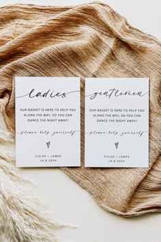 two white cards with black ink on them sitting on top of a brown and white blanket