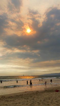 people are playing in the water at the beach as the sun sets over the ocean