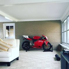 a red motorcycle parked in front of a brick wall next to a white couch and chair