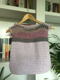 a crocheted sweater hanging on a wooden hanger in front of bookshelves