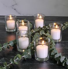 four candles are sitting on a table with greenery around them and one candle is lit