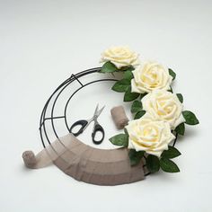 some fake flowers and scissors on a white table with black wire around the edges that have been cut out to make a wreath