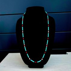 a necklace is displayed on a black display stand in front of a blue dresser with drawers