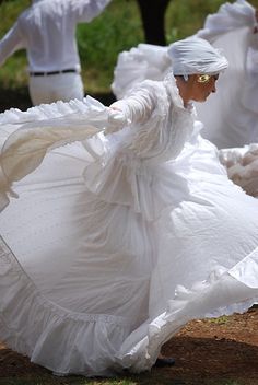 two people in white dresses and turbans are dancing with their arms spread out