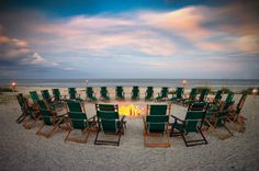 a fire pit surrounded by lawn chairs on the beach