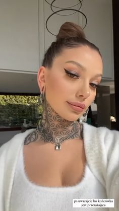 a woman with tattoos on her neck wearing a white sweater and silver hoop earring