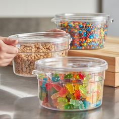 three plastic containers filled with gummy bears on top of a metal counter next to a wooden cutting board