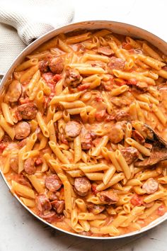 a skillet filled with pasta and meats on top of a white countertop