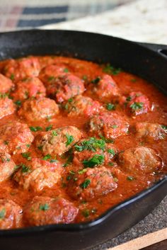 a skillet filled with meatballs covered in sauce and garnished with parsley