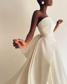 a woman in a white dress with her hand on her hip and wearing large earrings