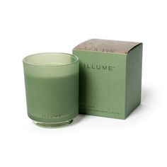 a green candle sitting next to a box on a white surface with the words illume written in it