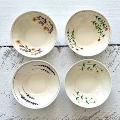 four white bowls with flowers painted on them sitting next to each other in front of a wall