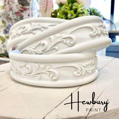 a white vase sitting on top of a table next to a potted plant in the background