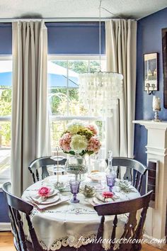 a dining room table set for two with flowers in vases on the table and chandelier hanging from the ceiling