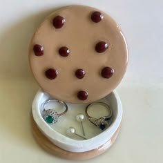 a ceramic ring box with two rings in it and some other jewelry on the lid