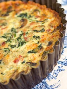 a quiche with cheese and spinach in a baking dish on a blue and white tablecloth