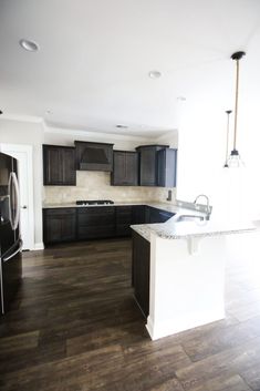 an empty kitchen with black cabinets and white counter tops, dark wood flooring and stainless steel appliances