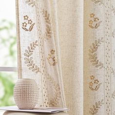 a white vase sitting on top of a table next to a window covered in curtains