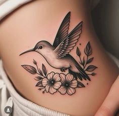 a woman's stomach with a bird and flowers tattoo on her side ribcage