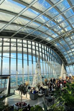 the inside of a building with lots of plants and people standing around looking out at the city