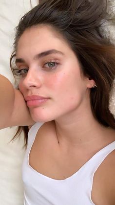 a young woman laying on top of a bed next to a white wall with her hand under her chin