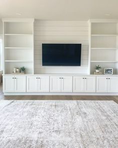 a living room with white bookcases and a flat screen tv mounted on the wall