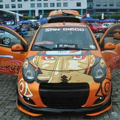 an orange car with anime characters painted on it's hood and side windows, parked in a parking lot next to other cars