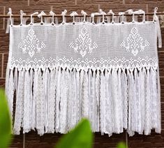 a white crochet curtain hanging on a brick wall next to green plants and leaves