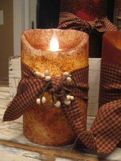 a lit candle sitting on top of a wooden table next to two wrapped candles with bows