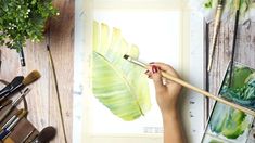 a person holding a paintbrush in their hand next to some art supplies on a table