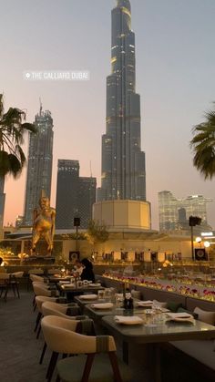 an outdoor dining area with tables and chairs in front of the burj building