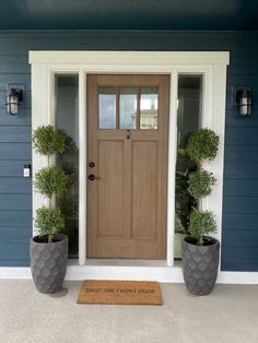 two potted plants sit on the front porch of a house with a welcome mat