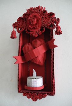 a red box with a candle and some paper on the inside that is cut out to look like roses