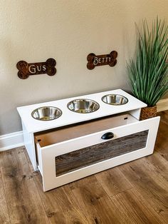 the dog bowl stand has two bowls on it and is made out of white wood