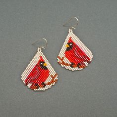 a pair of red and white beaded earrings with a cardinal on the front, sitting on a gray surface