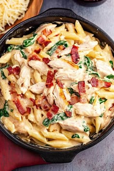 a skillet filled with pasta, chicken and spinach on top of a table