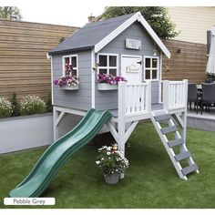 a play house with a slide and flower pots on the grass in front of it