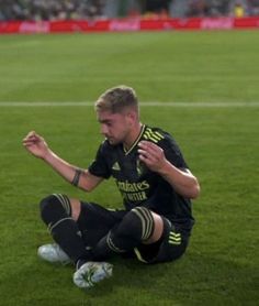 a soccer player sitting on the ground with his foot in the air and looking down