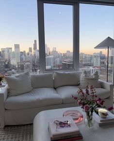 a living room filled with white furniture and tall windows overlooking the cityscape in the distance