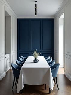 a dining room table with blue chairs and a white table cloth on it in front of a dark blue paneled wall